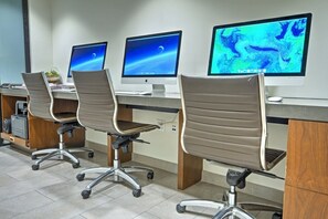 Une rangée de chaises de bureau à roulettes, un bureau avec un écran d’ordinateur et une imprimante posée sur une étagère.