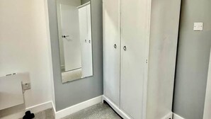 Een kamer met een grijs vloerkleed, een witte kast en een spiegel aan de muur.
