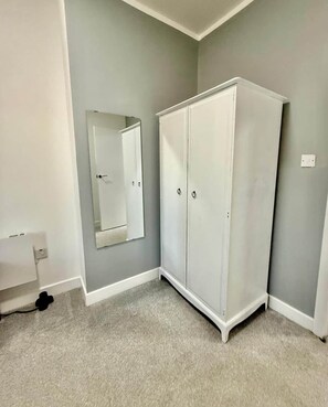 Ein Zimmer mit grauem Teppich, einem weißen Wandschrank und einem Spiegel an der Wand.