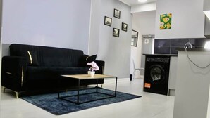 Een moderne woonkamer met een zwarte bank, een bijzettafeltje en een wasmachine op de achtergrond.