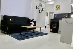 Ein modernes Wohnzimmer mit einem schwarzen Sofa, einem Couchtisch und einer Waschmaschine im Hintergrund.