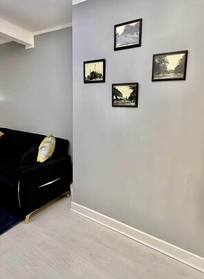 A room with a grey wall, a black sofa with a cushion, and four framed pictures. - Bright, Modern & Comfortable 2-Bedroom Apartment (Manchester)