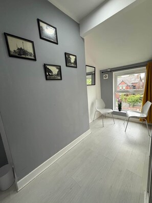 A room with grey walls, a large window with curtains, and a white chair. - Bright, Modern & Comfortable 2-Bedroom Apartment (Manchester)