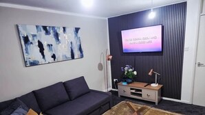 En moderne stue med en mørk sofa, et sofabord, et fladskærms-tv og en dekorativ vægdekoration.