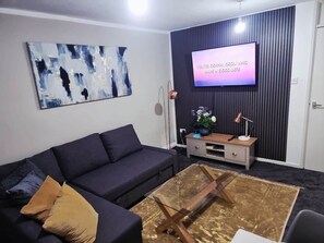 Ein modernes Wohnzimmer mit einem dunklen Sofa, einem Couchtisch, einem Flachbildfernseher und einer Wanddekoration.