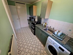 Une cuisine de taille réduite équipée d’un lave-linge, d’un évier et d’une cuisinière.
