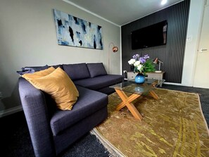 Un salon moderne avec un canapé d’angle, une table basse en verre et un téléviseur à écran plat fixé au mur.