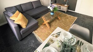 En moderne stue med en sofa, et sofabord og et spiseområde med tallerkener og glas.