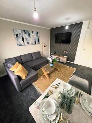 Ein modernes Wohnzimmer mit einer Couch, einem Couchtisch und einem Essbereich, gedeckt mit Tellern und Gläsern.
