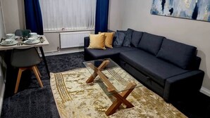 En stue med en mørk sofa, et glasbord, et spisebord med tallerkener og en blå gardin.