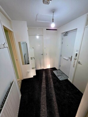 Un couloir avec un tapis noir, des murs blancs et un luminaire au plafond.