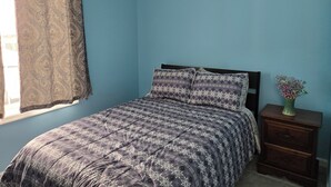 Ein Schlafzimmer mit Bett, Nachttisch, Fenster mit Vorhang und Wandlüfter.