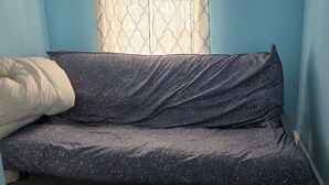Ein Zimmer mit einem Einzelbett, einem Fenster mit gemusterten Vorhängen und einem Deckenventilator.