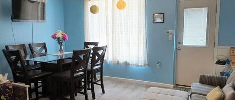 Un comedor con una mesa y sillas, un ventilador de techo, una ventana con cortinas y una puerta con ventanal.