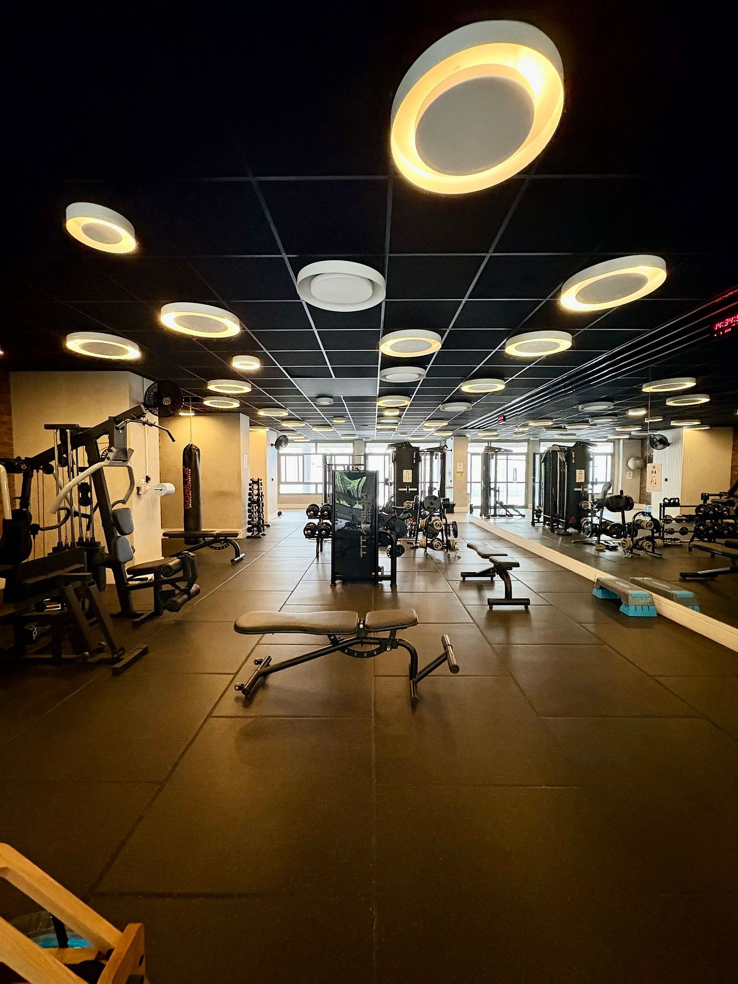 Un gimnasio con varias máquinas de ejercicio, una banca y luces circulares en el techo.