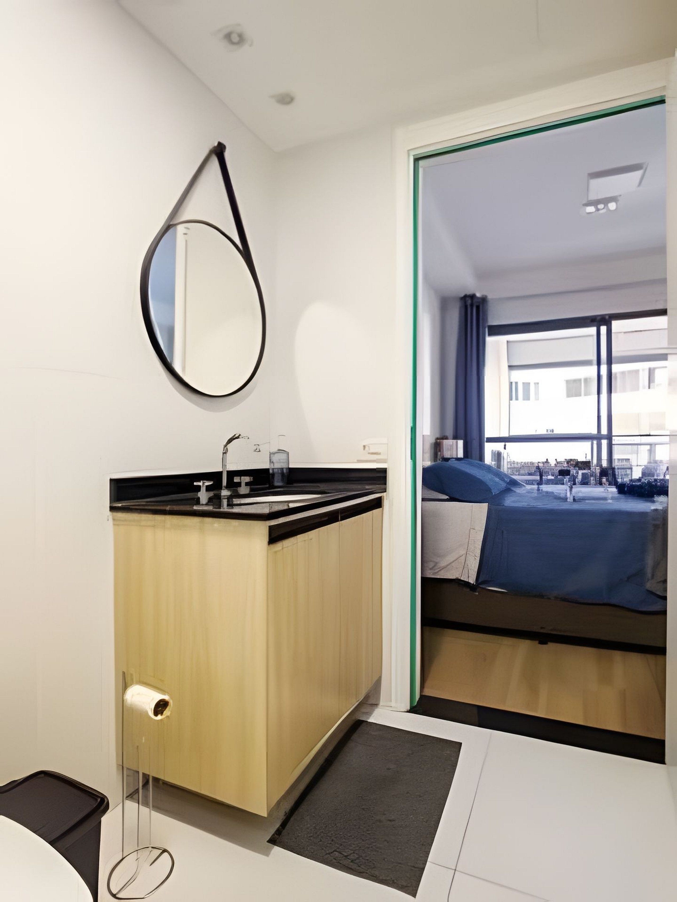 Een moderne hotelkamer met een houten opbergmeubel, een spiegel, een bed met een blauwe deken, en uitzicht op de stad door het raam.