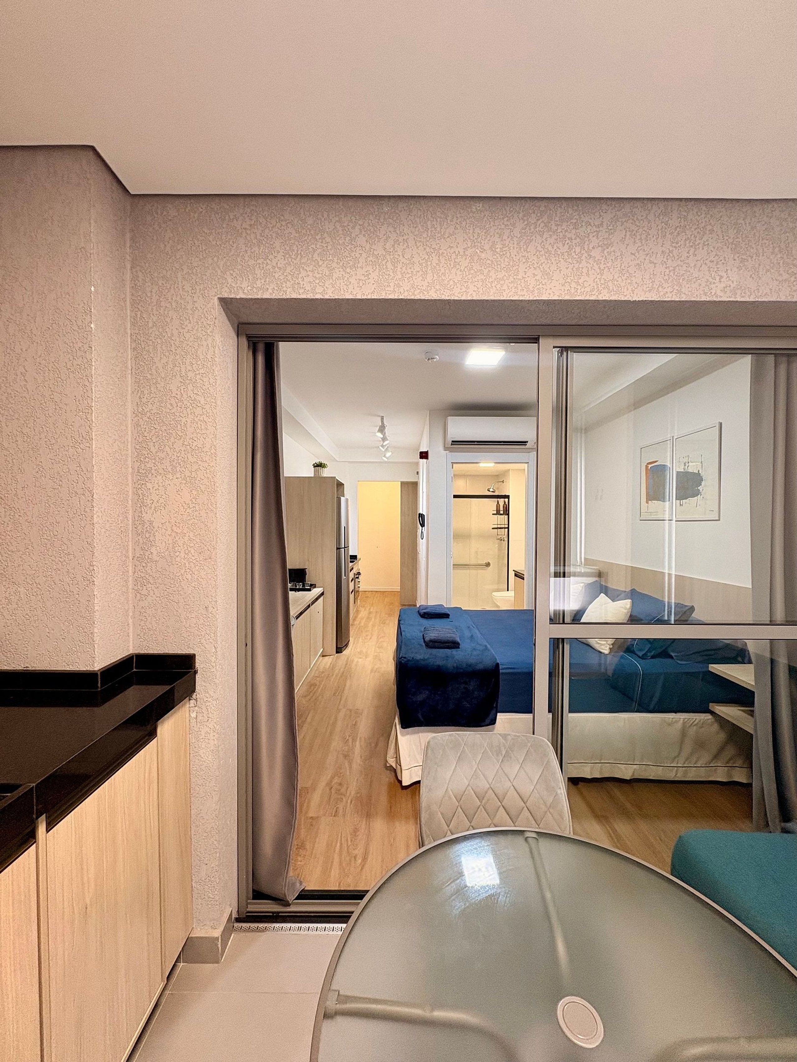 Ein Hotelzimmer mit Küchenzeile, einem Bett, einem Glastisch und einem durchgegangene Tür erkennbaren Badezimmer.