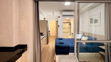 Ein Hotelzimmer mit Küchenzeile, einem Bett, einem Glastisch und einem durchgegangene Tür erkennbaren Badezimmer.