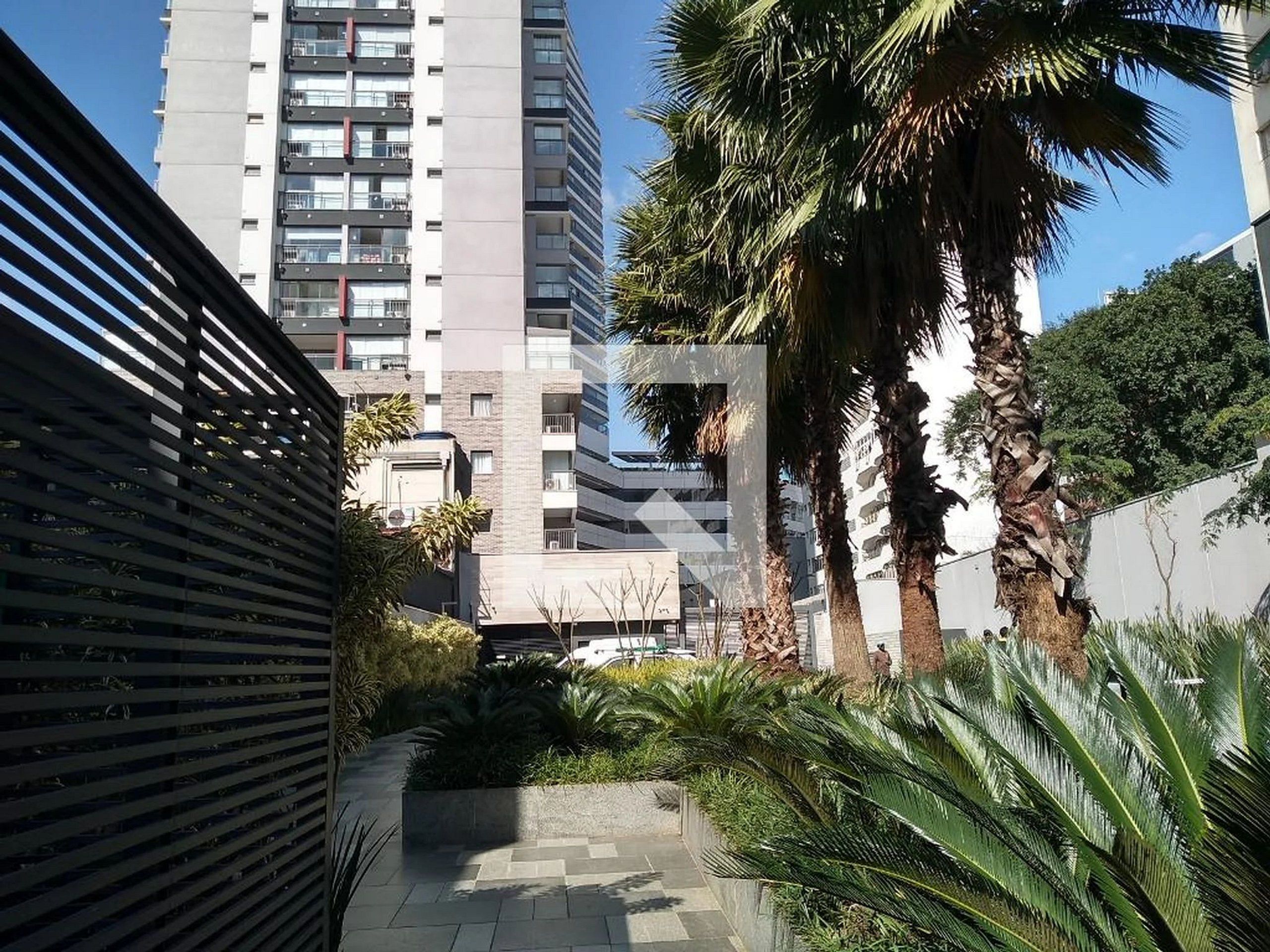 Un sendero urbano moderno con una valla metálica, palmeras y un edificio alto al fondo.