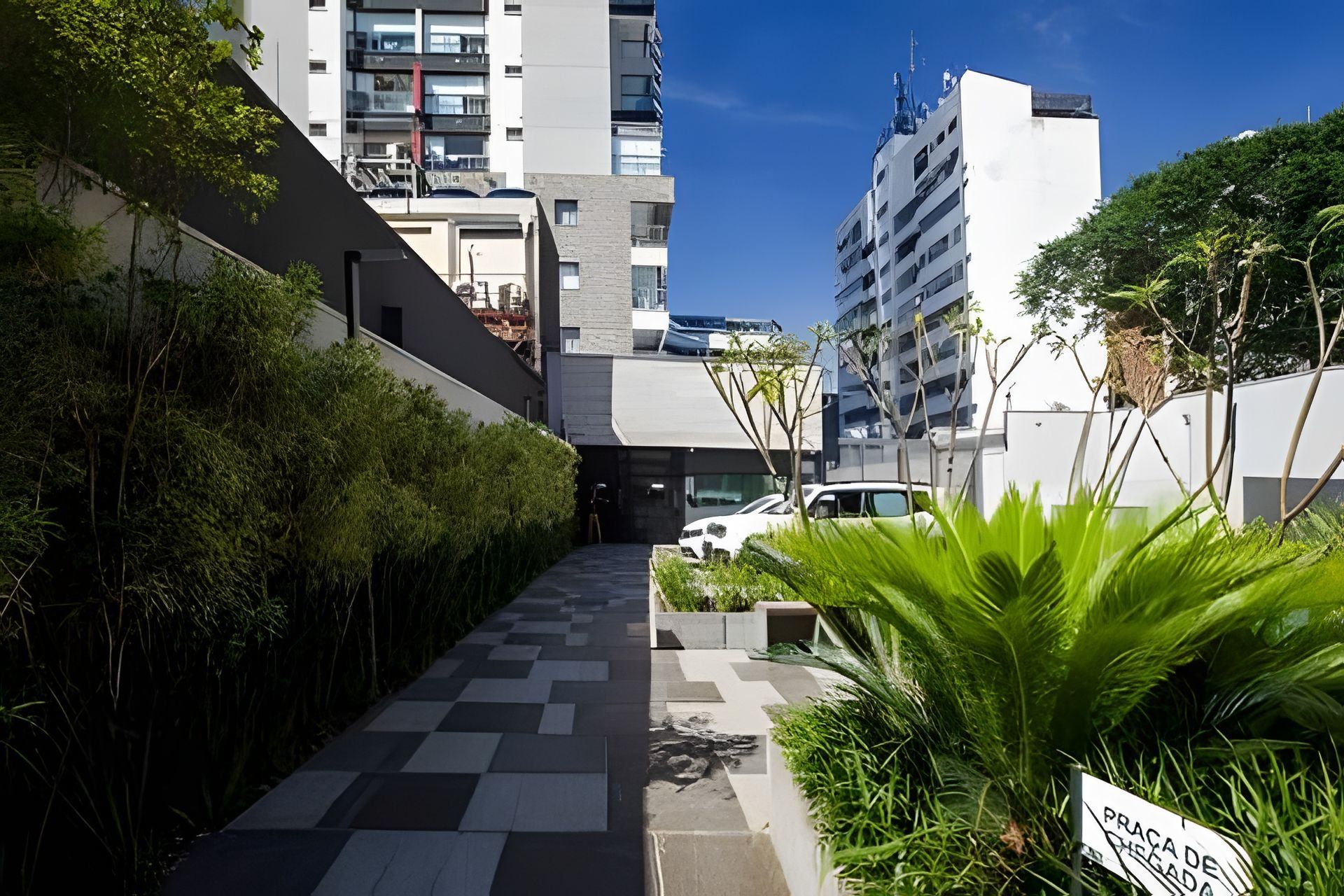 A pathway leading to a building with a modern design, surrounded by greenery and a clear sky.