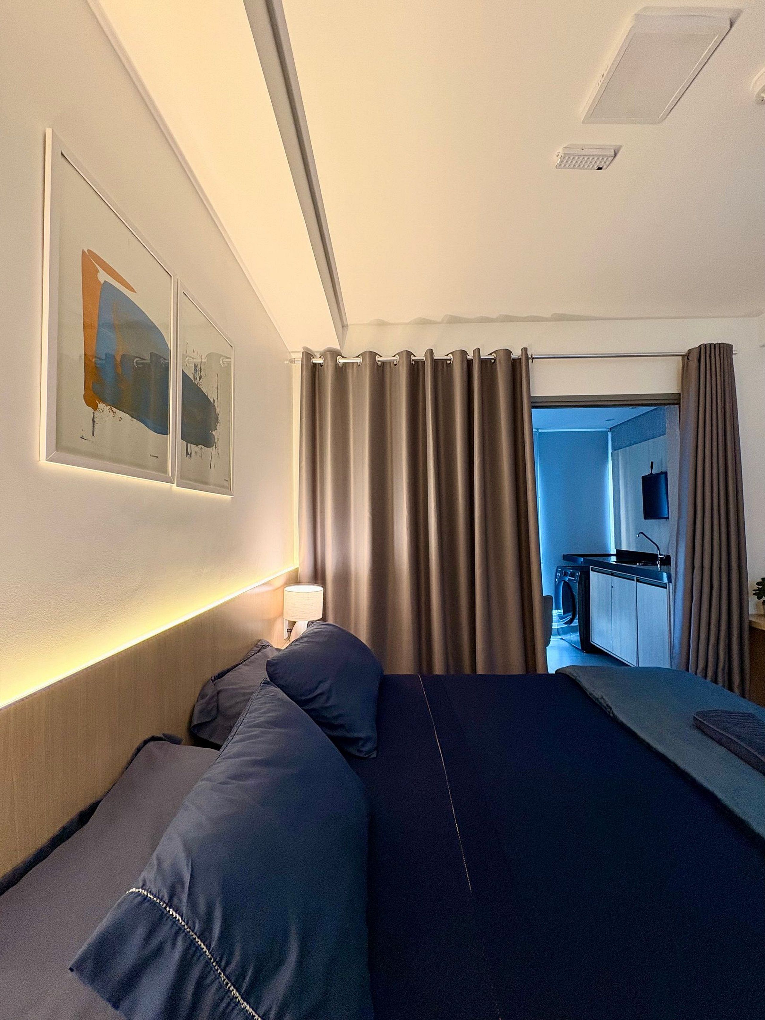 A hotel room with a bed, a desk, a washing machine, and a wall-mounted artwork.