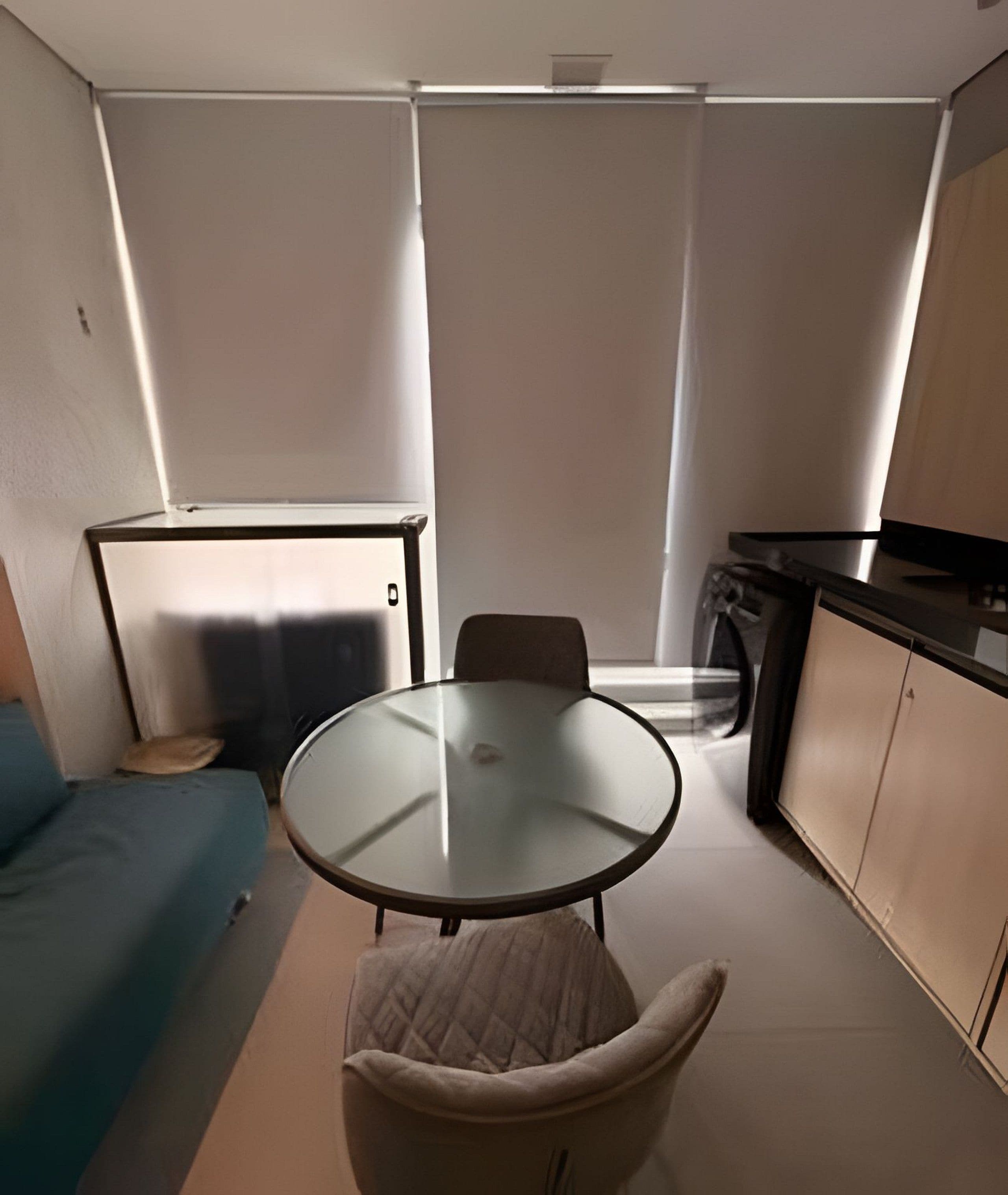 Um espaço compacto para viver, com cozinha americana, mesa redonda de vidro, sofá e cama para animais de estimação.