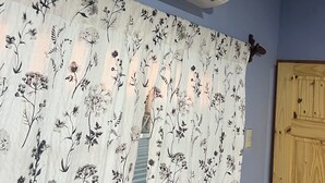 Um quarto com cortina de padrão floral, porta de madeira e ar-condicionado fixado na parede.