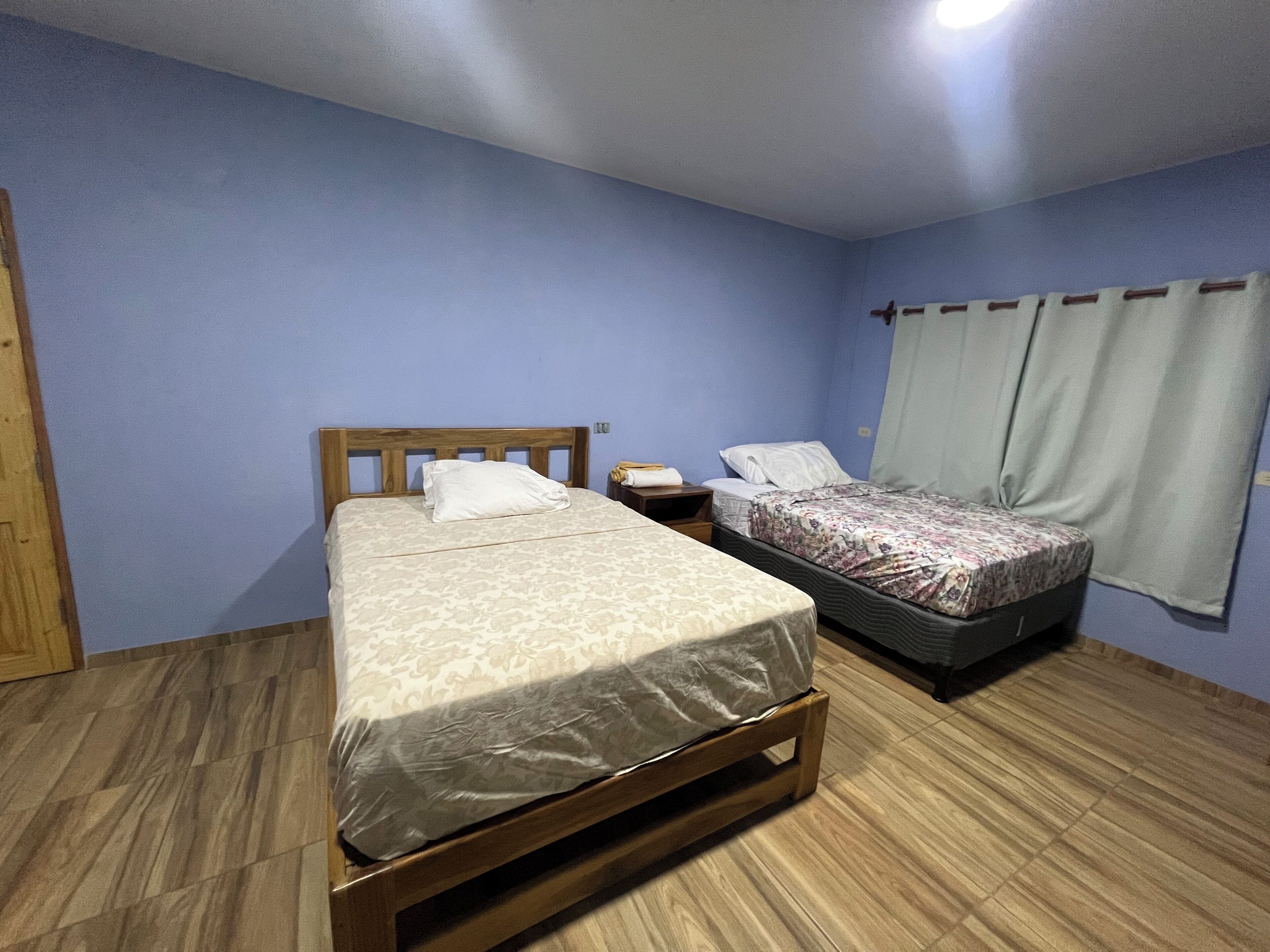 Slaapkamer met twee bedden, houten hoofdborden, een nachtkastje en een raam met gordijnen.