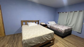 Slaapkamer met twee bedden, houten hoofdborden, een nachtkastje en een raam met gordijnen.