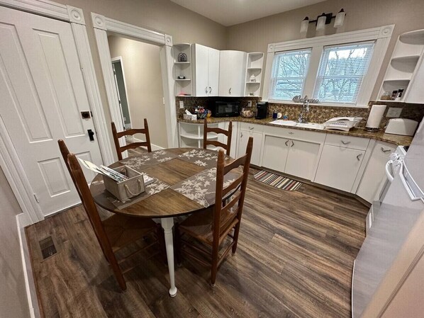 A kitchen with a dining table, chairs, cabinets, a microwave, and a window.