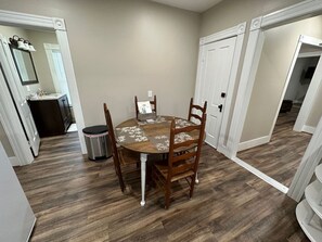 A dining area with a round table and chairs, a trash can, and a kitchen in the background.