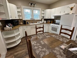 A kitchen with white cabinets, a granite countertop, a dining table with chairs, and a refrigerator.