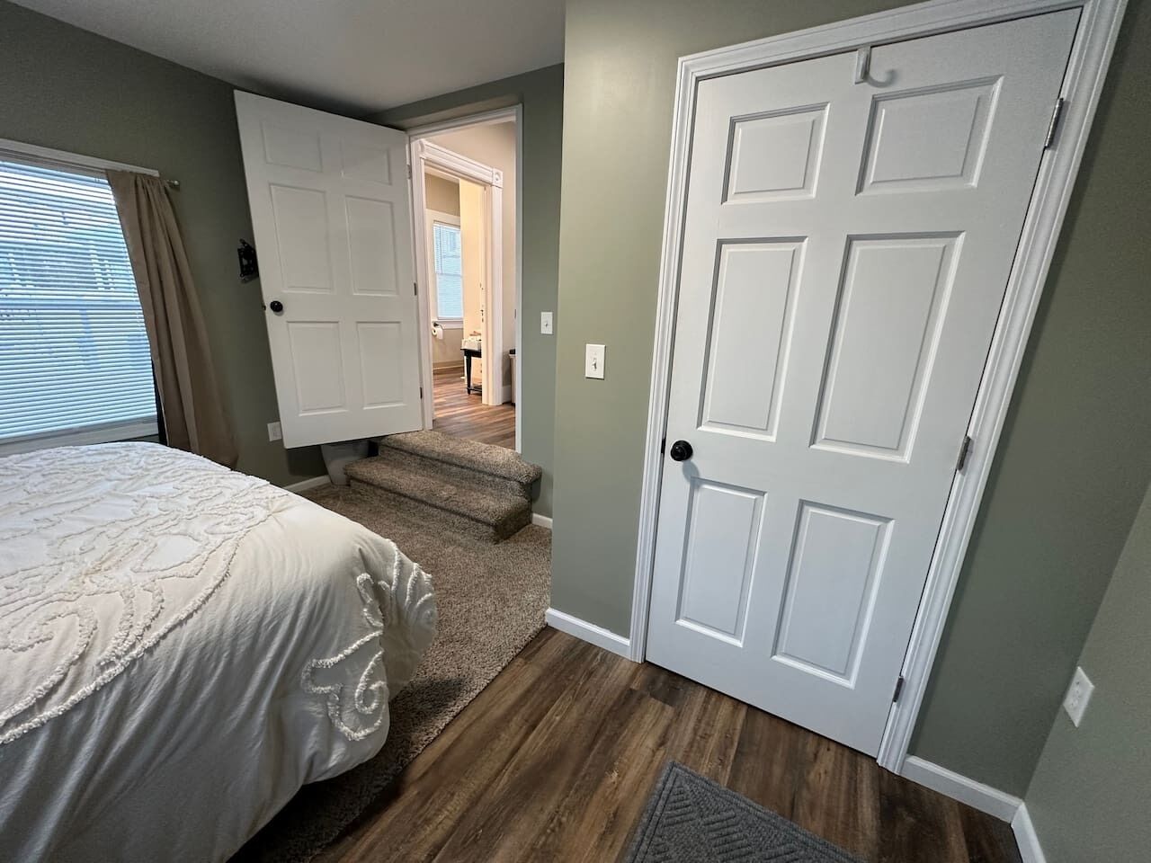 A bedroom with a bed, a door, and a staircase leading to another room.
