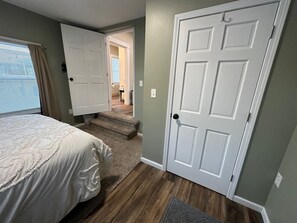 A bedroom with a bed, a door, and a staircase leading to another room.