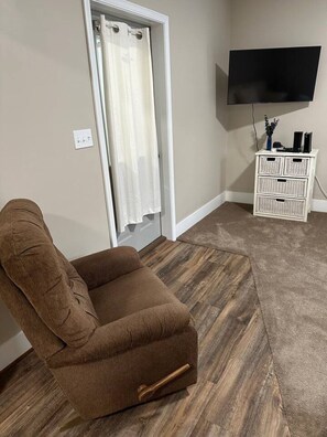 A room with a brown chair, a television on the wall, and a white storage unit.