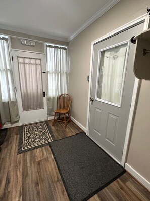A hallway with a wooden floor, a rug, a chair, and two doors with curtains.