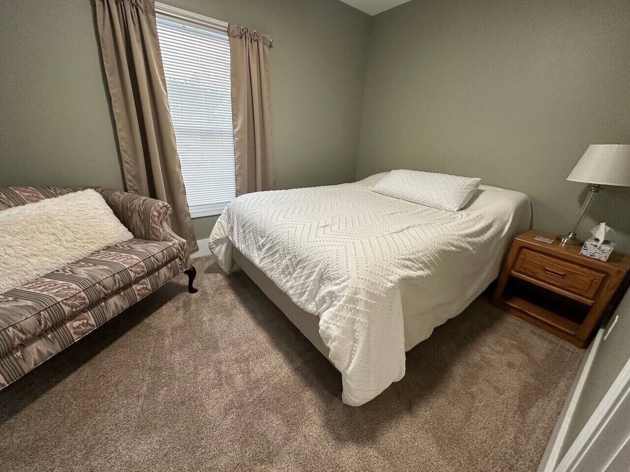 Un dormitori amb un llit, un sofà, una camabaixa i una finestra amb cortines.