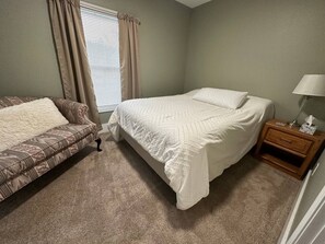 A bedroom with a bed, a sofa, a nightstand, and a window with curtains.