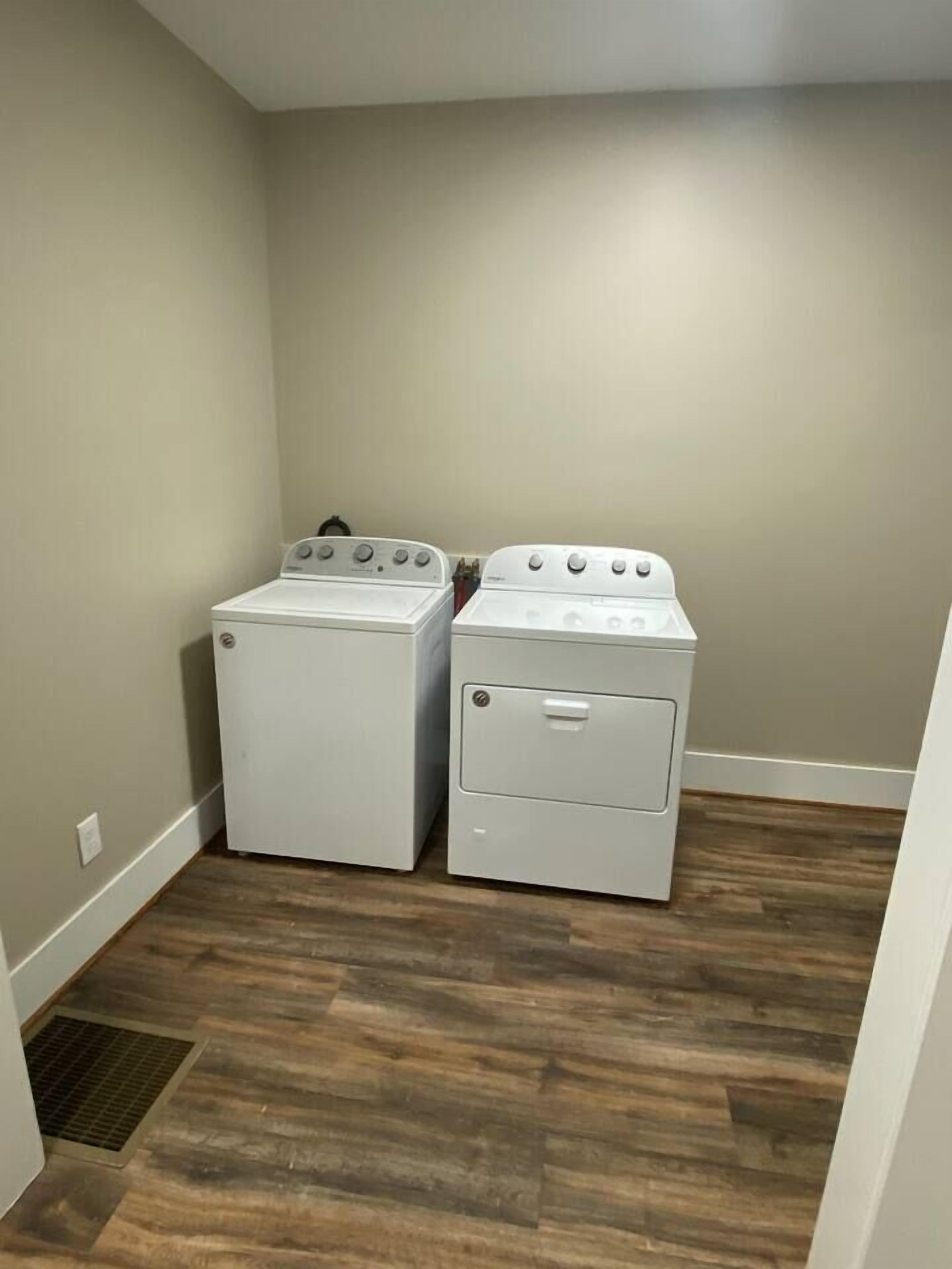 Una sala amb rentadora i assecadora, sòl de fusta i un ventilador.