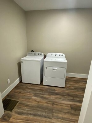 A laundry room with a washer and dryer, wooden flooring, and a vent.