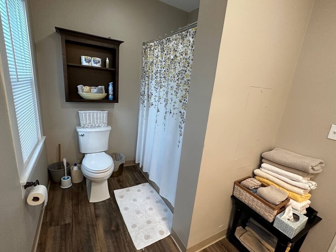 A bathroom with a toilet, a shower curtain, a sink, and a stack of towels.