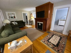Una sala de estar con sofá, una mesa de centro, chimenea y televisión montada en la pared.
