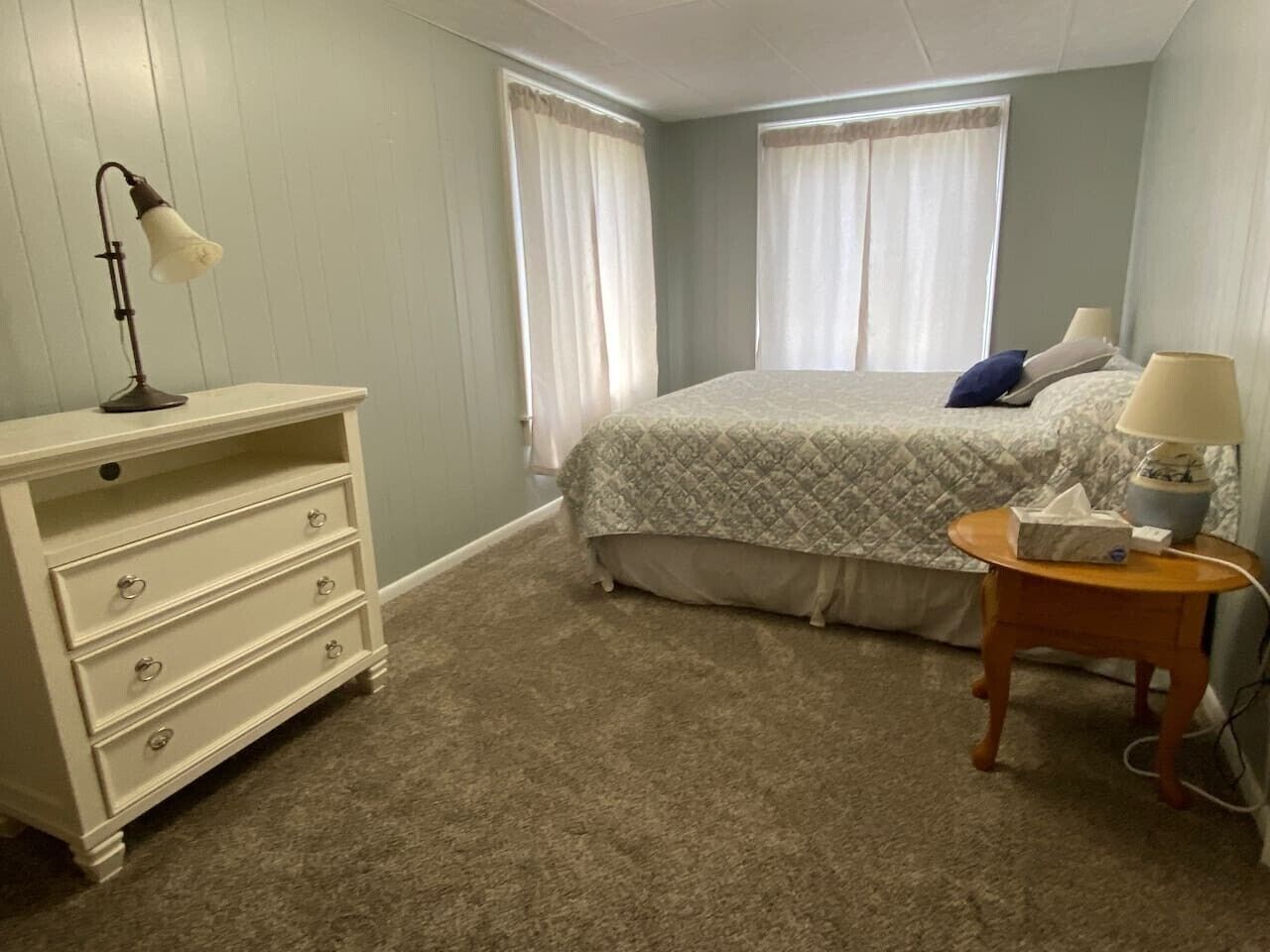 Une chambre à coucher avec un lit, une commode, une lampe et une table de chevet.