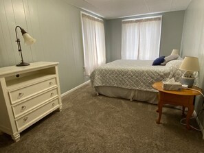 Un dormitorio con cama, cómoda, lámpara y mesita de noche.