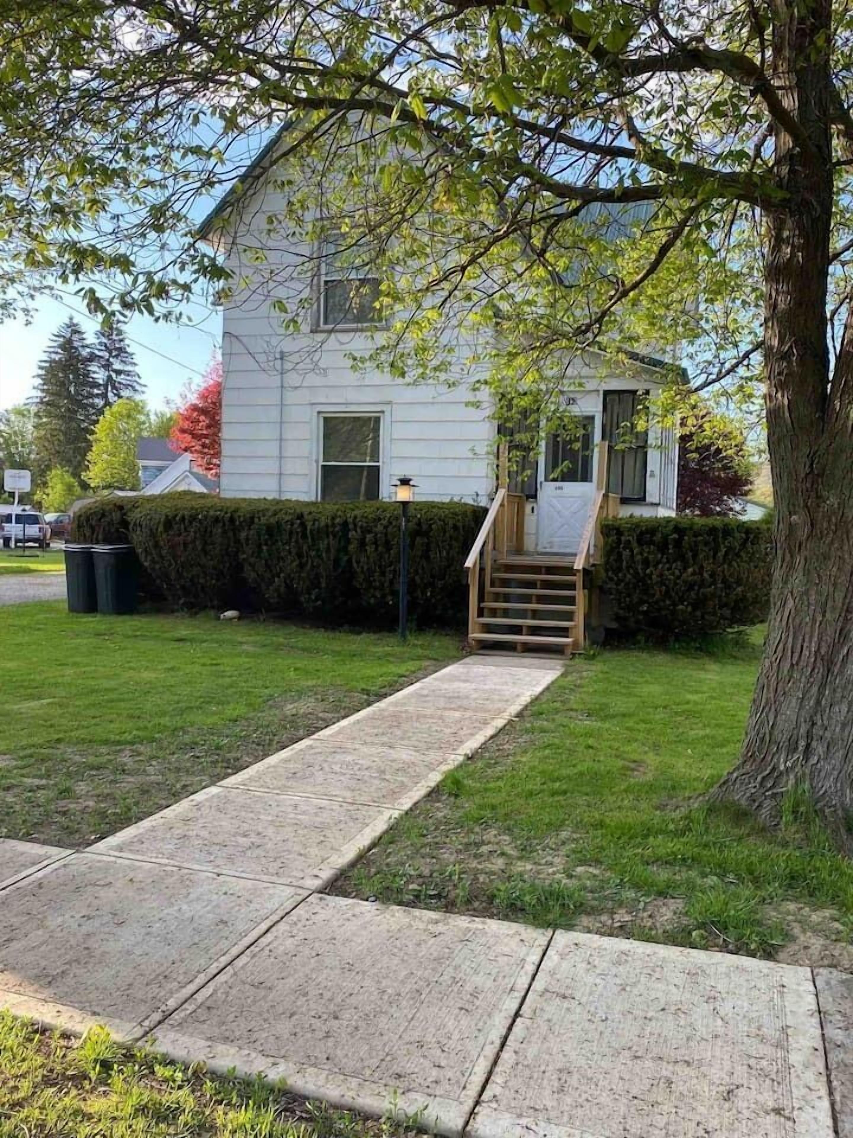 Une maison avec un jardin devant, un escalier en bois et une haie.