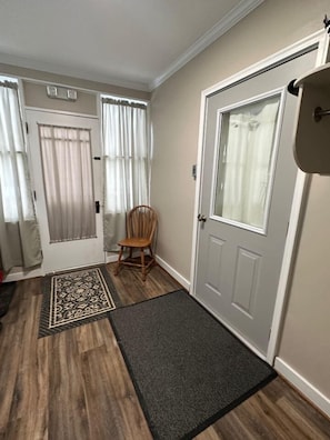 Un couloir avec un plancher en bois, un tapis, une chaise et deux portes avec des rideaux.