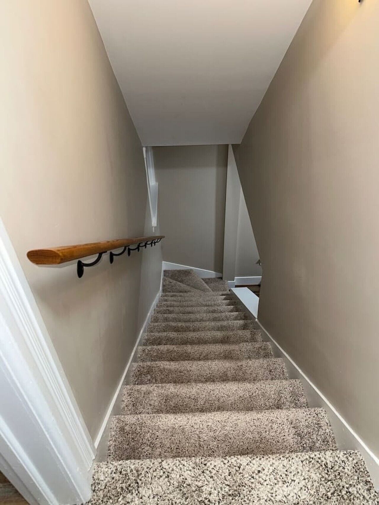 Un escalier recouvert de moquette, avec une main courante sur le côté gauche et un mur blanc sur le côté droit.