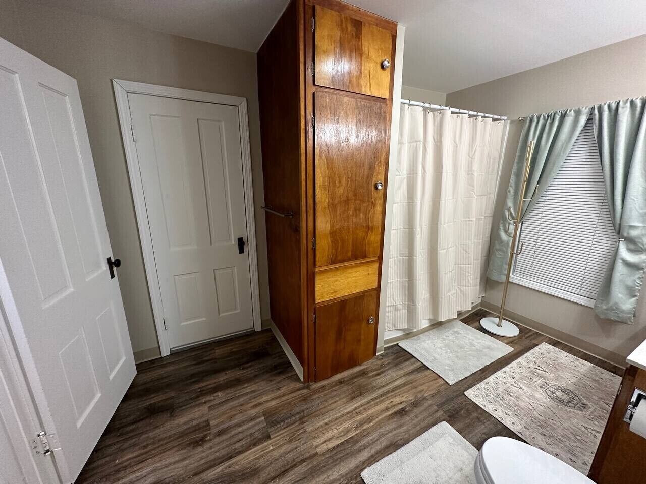 Une salle de bain avec un meuble en bois, des toilettes, un bidet, un rideau de douche et un tapis de sol.