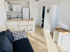 A compact living space with a kitchenette, a sofa with patterned cushions, and a door leading to another room. - Apartment in Salou, 2 minutes from the beach (Salou)