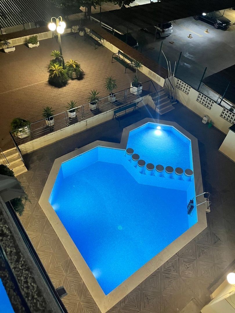 A swimming pool with a geometric shape, surrounded by a tiled deck and a railing.